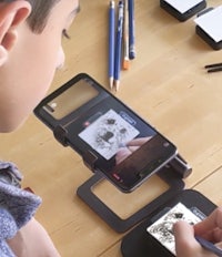 a boy is using a smartphone to draw on a table